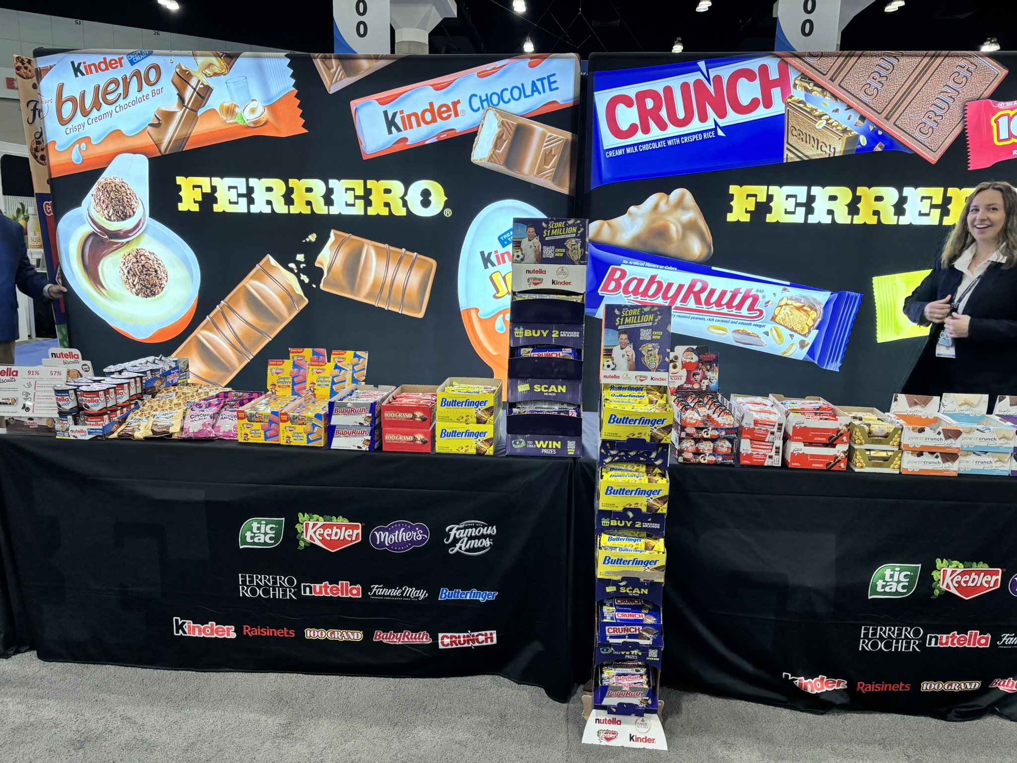 Ferrero booth with lit Kinder Bueno, Crunch and Baby Ruth graphics above a black table skirt of candy brand logos.