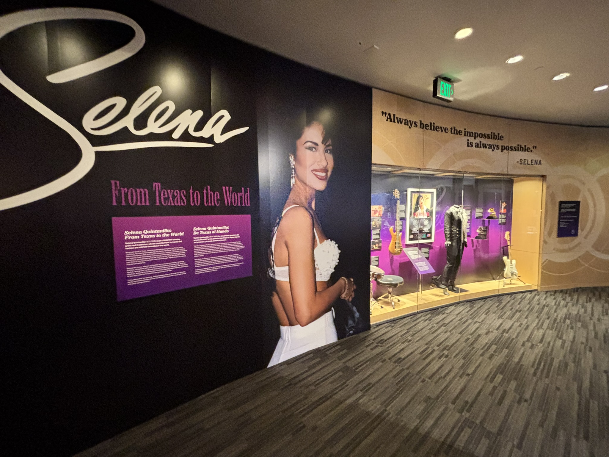 Museum wall with a large portrait and the text Selena From Texas to the World, beside a lit display case.