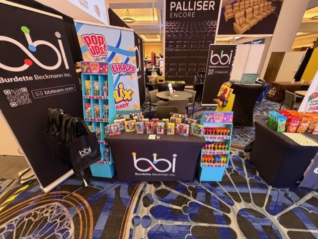 bbi booth with banner stands, Pop Ups and Lip Pops lollipop displays and a black bbi table cover on patterned carpet.