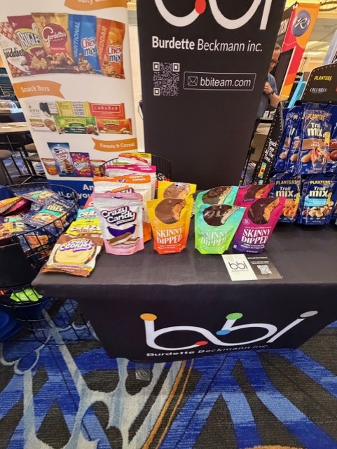 Crazy Candy, Skinny Dipped and cookie snack packs on a black bbi table in front of a snack bars banner.