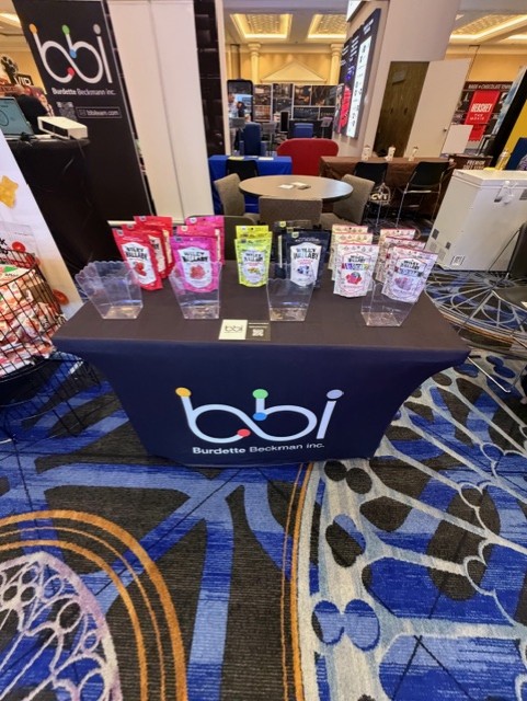 Candy pouches in clear holders on a black bbi table cover, with a bbi banner behind.