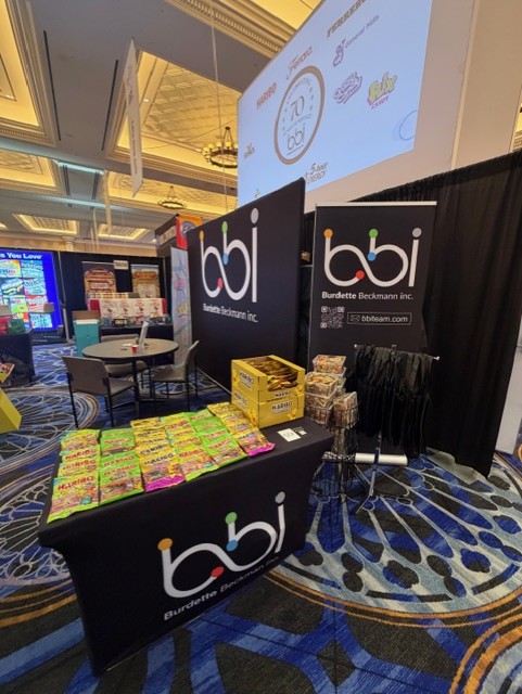bbi booth with Haribo gummy candy on a black bbi table, bbi banners and a screen showing a bbi 70th anniversary logo.