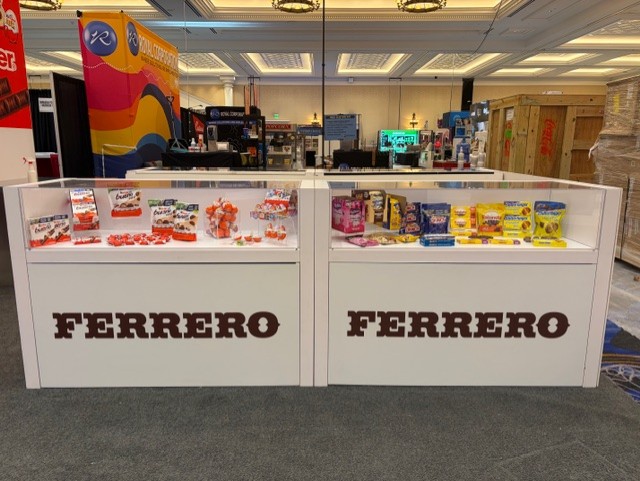 Two white Ferrero display counters holding Kinder and other candy under glass in a convention ballroom.