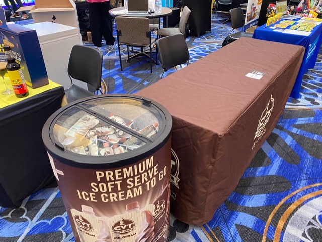 Brown CVT Premium Soft Serve Ice Cream To Go freezer and table cover at a trade show booth.
