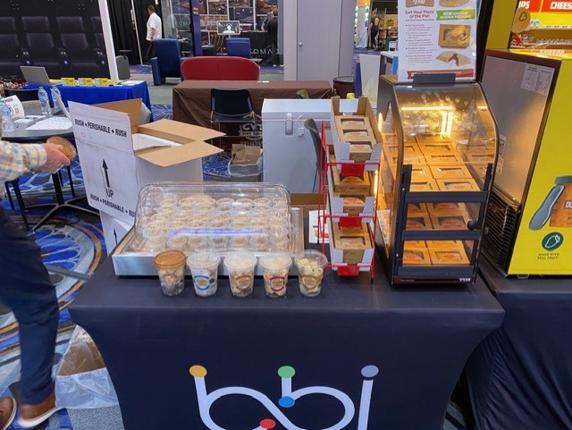 Dessert cups, boxed baked items in a heated display case and a rush perishable box on a black bbi table.