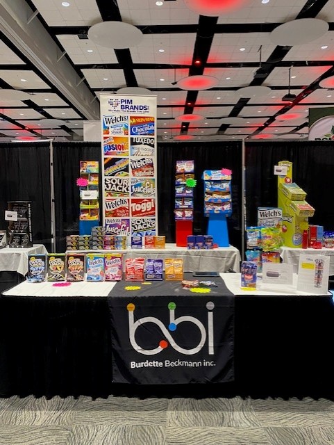 bbi booth table with a PIM Brands banner of Welch's and Sour Jack snacks and rows of boxed candy.