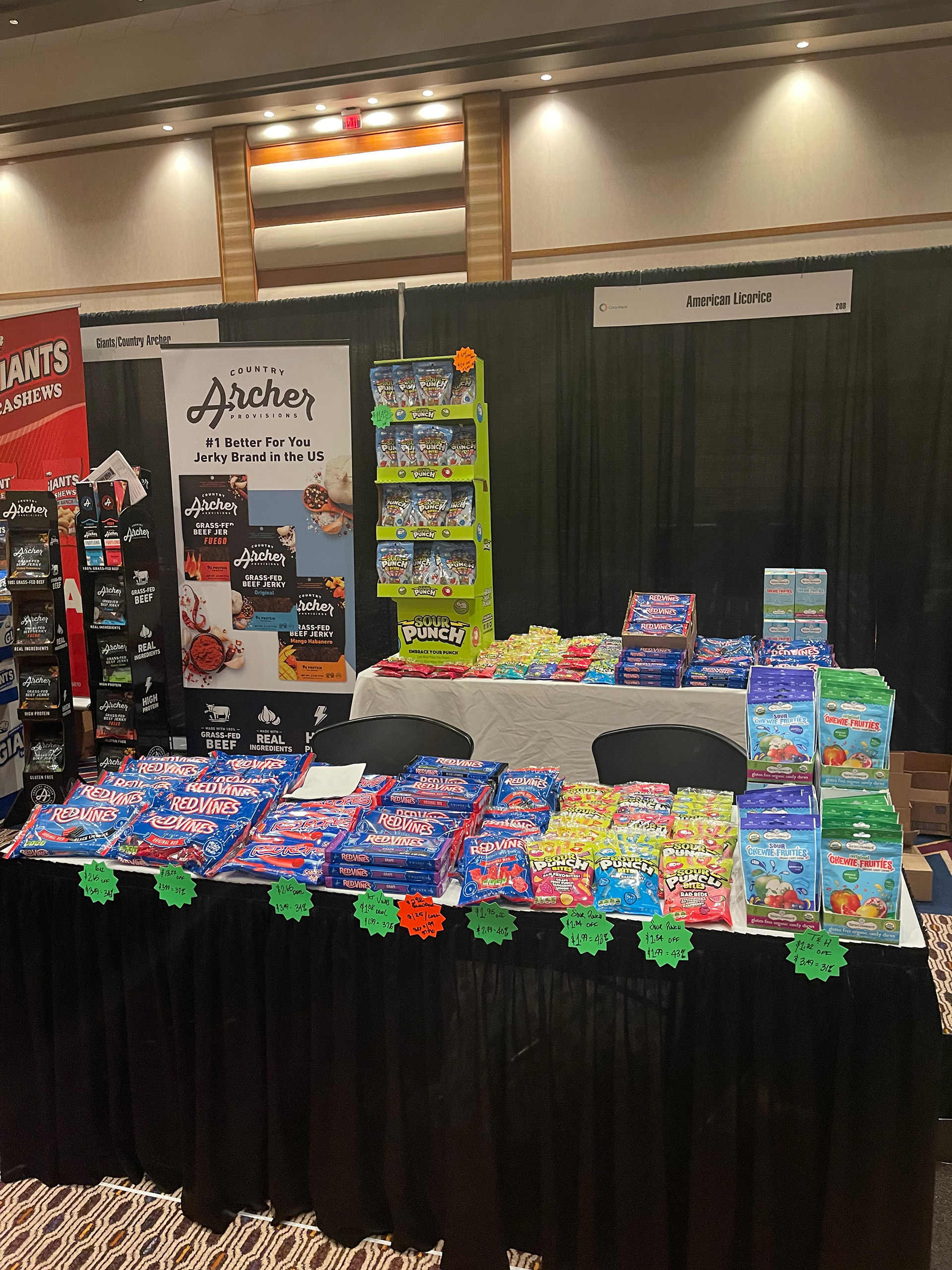 Table of Red Vines, Sour Punch and fruit snack packs beside a Country Archer jerky banner and an American Licorice sign.