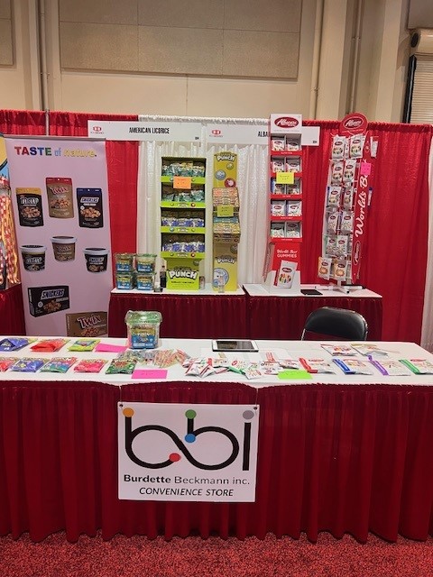 Unstaffed booth with a bbi Convenience Store sign, a Taste of Nature banner and Sour Punch and Albanese displays.