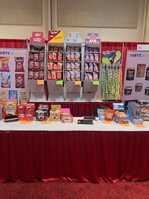Unstaffed booth with cotton candy displays, Cookie Dough Bites and a Taste of Nature banner behind a red-skirted table.