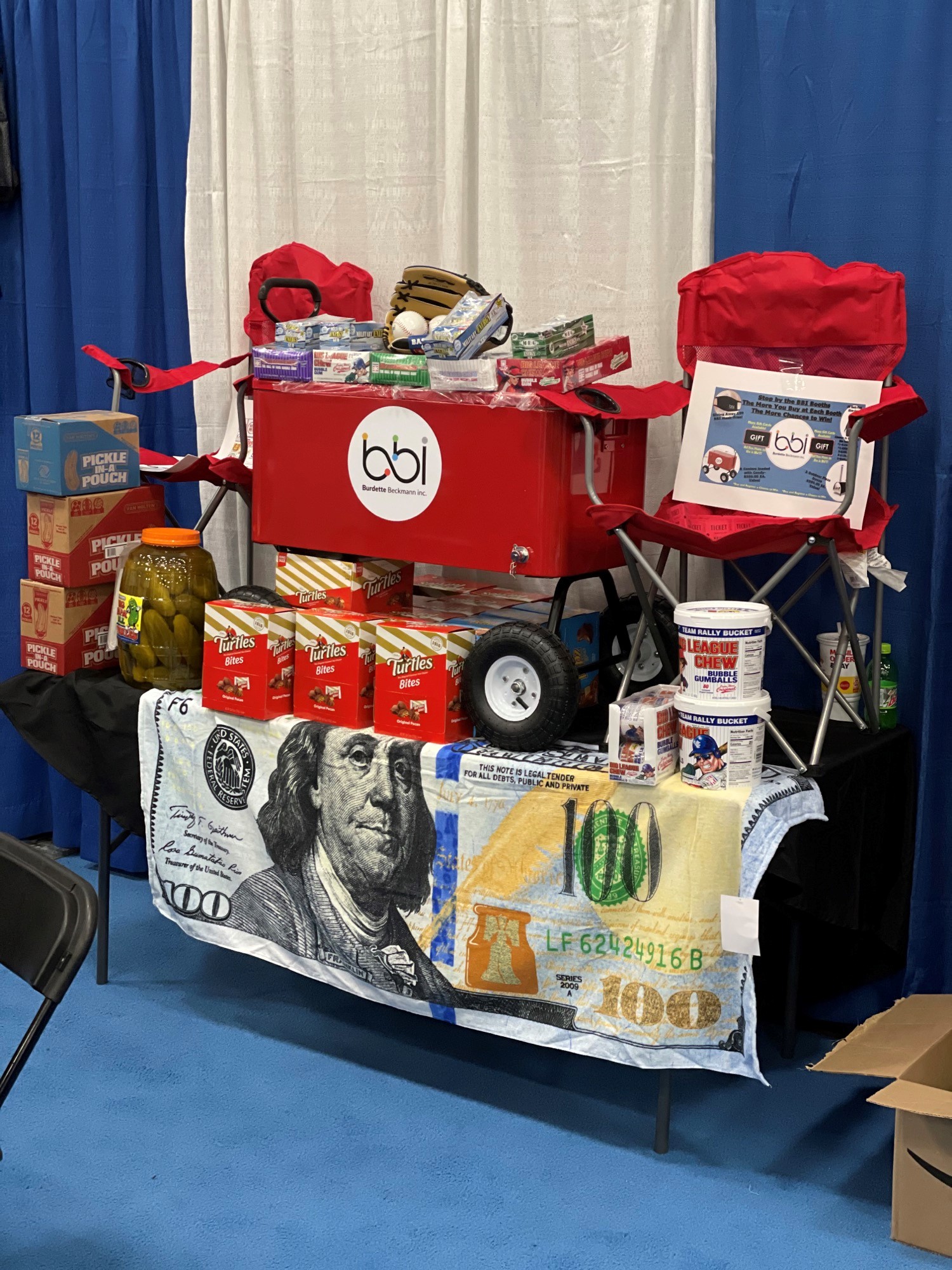 Close view of the red bbi wagon cooler with Turtles Bites boxes, a jar of pickles and a dollar-bill tablecloth.