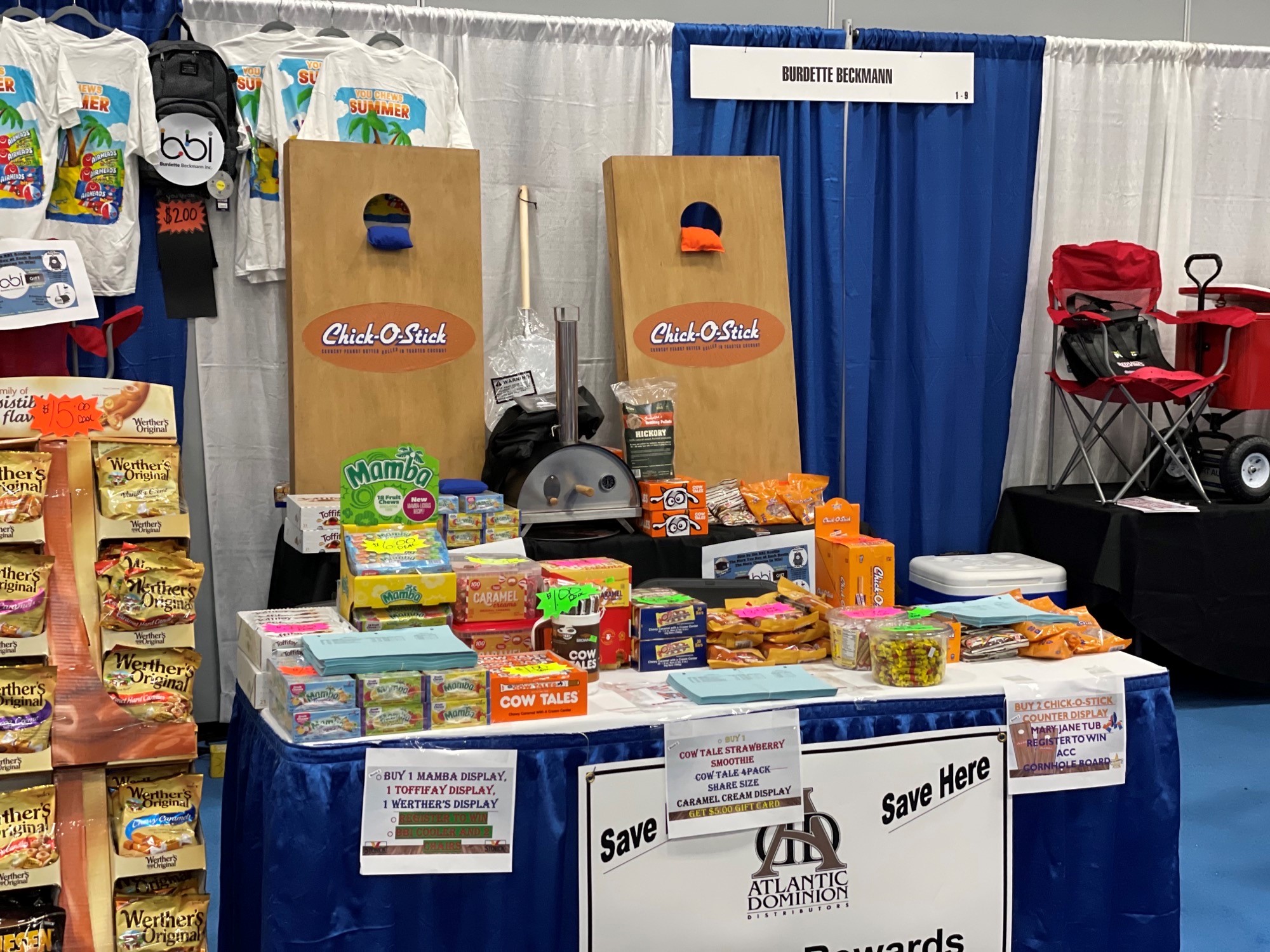 Booth with two Chick-O-Stick cornhole boards, a Werther's Original display and summer T-shirts above a candy-covered table.