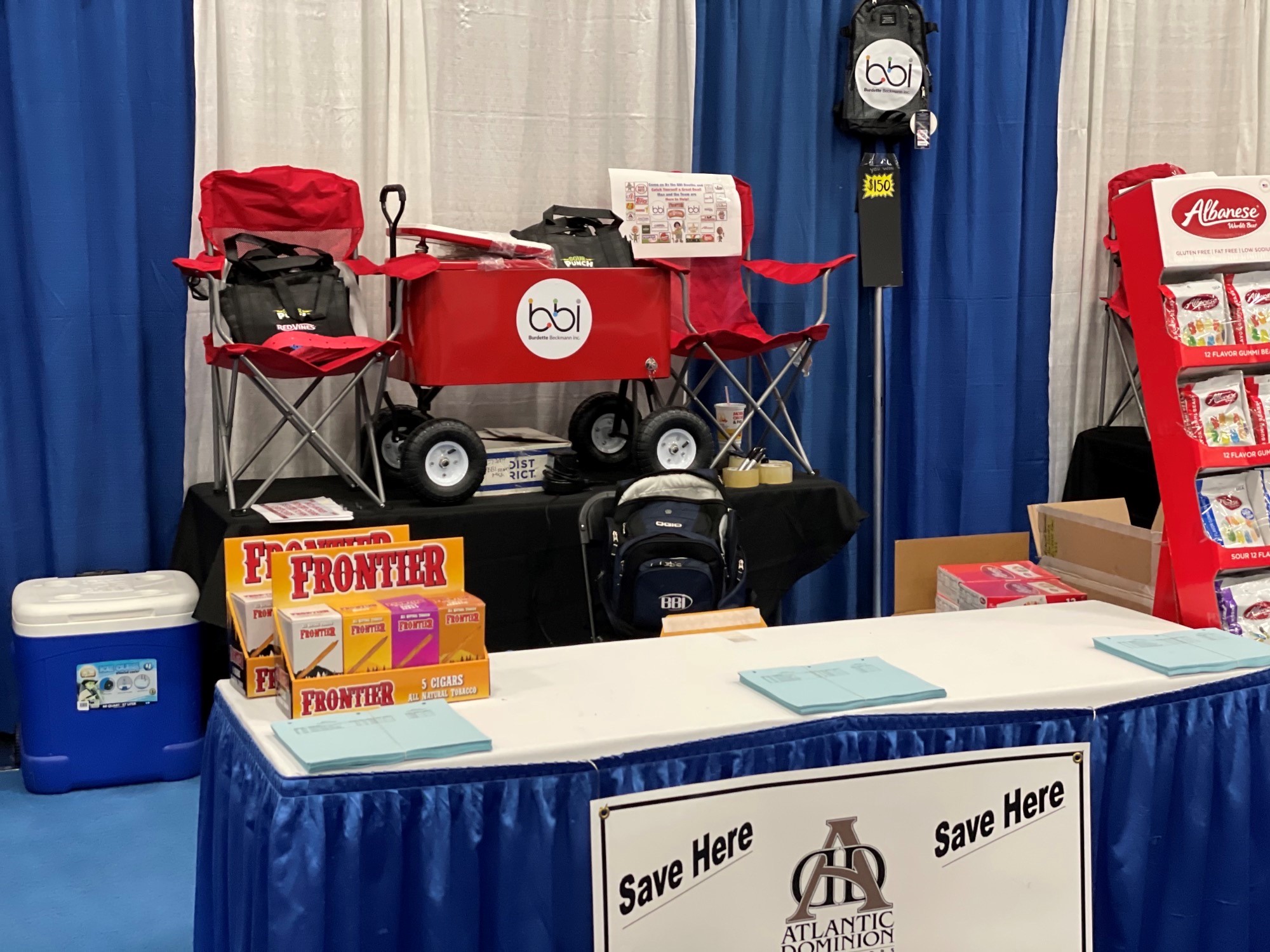 Red bbi wagon cooler on a black-draped table beside Frontier cigar boxes and a booth sign reading Save Here.