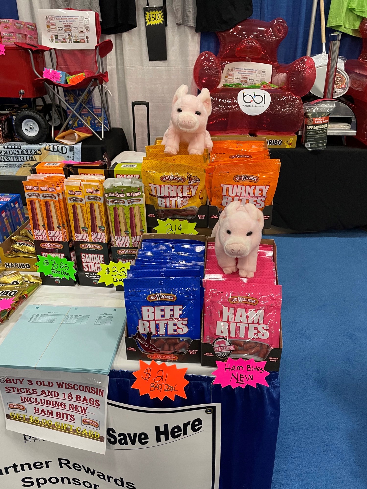 Old Wisconsin beef, turkey and ham bites packs with two plush pigs, in front of a red inflatable chair marked bbi.
