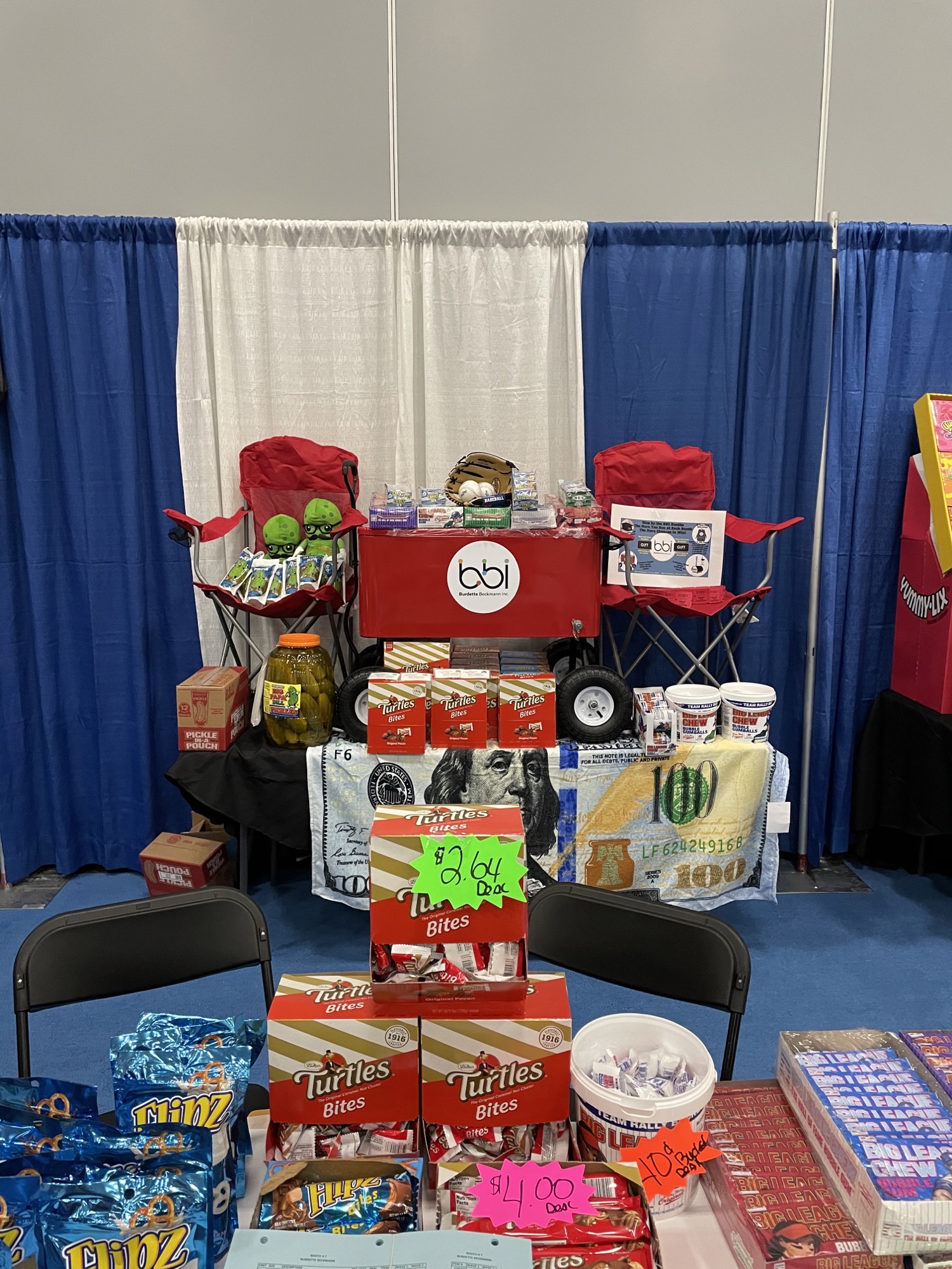 Red bbi wagon cooler between two red chairs, with Turtles Bites boxes and a dollar-bill tablecloth above Flipz pretzels.