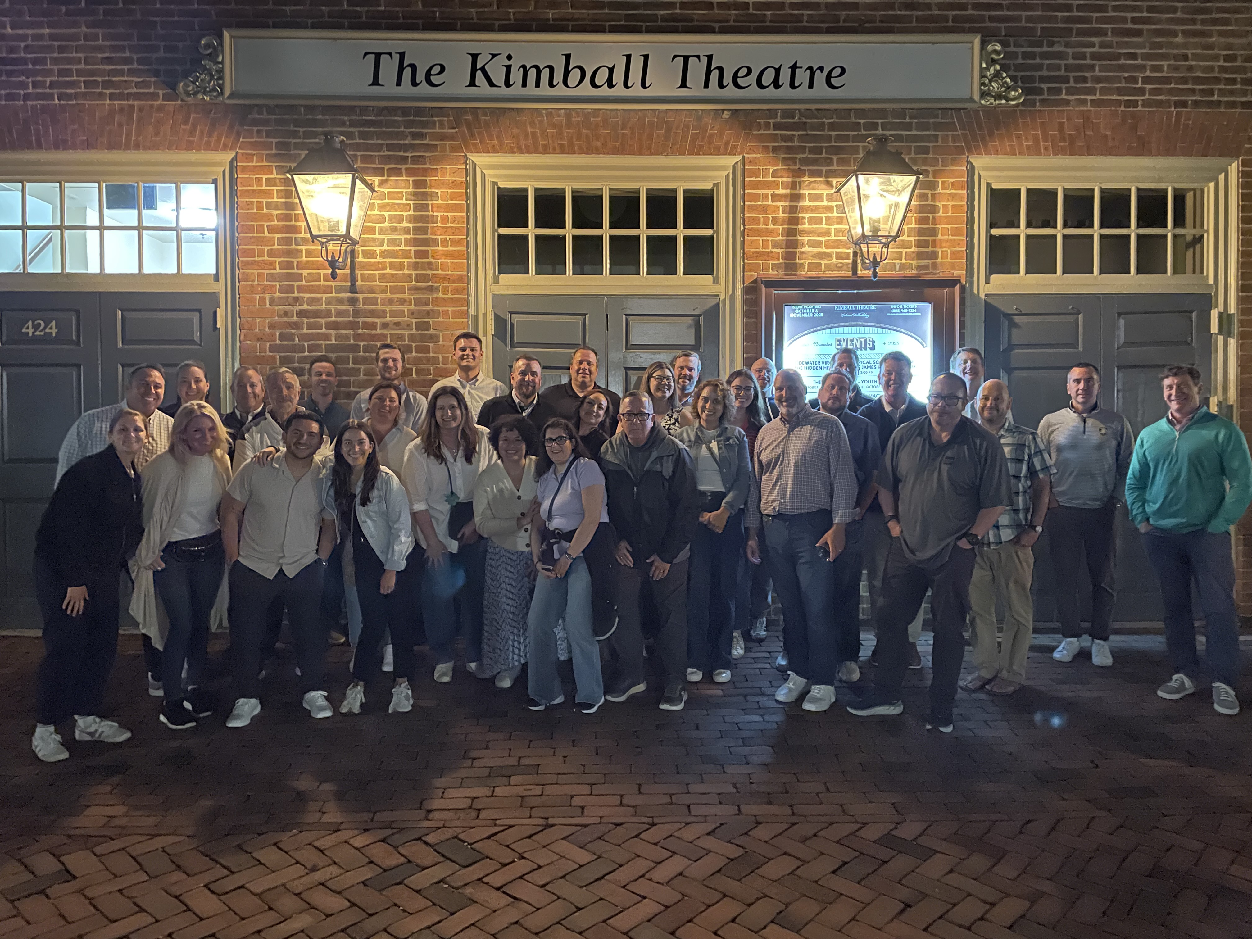 Large group poses at night beneath a sign reading The Kimball Theatre on a brick building.