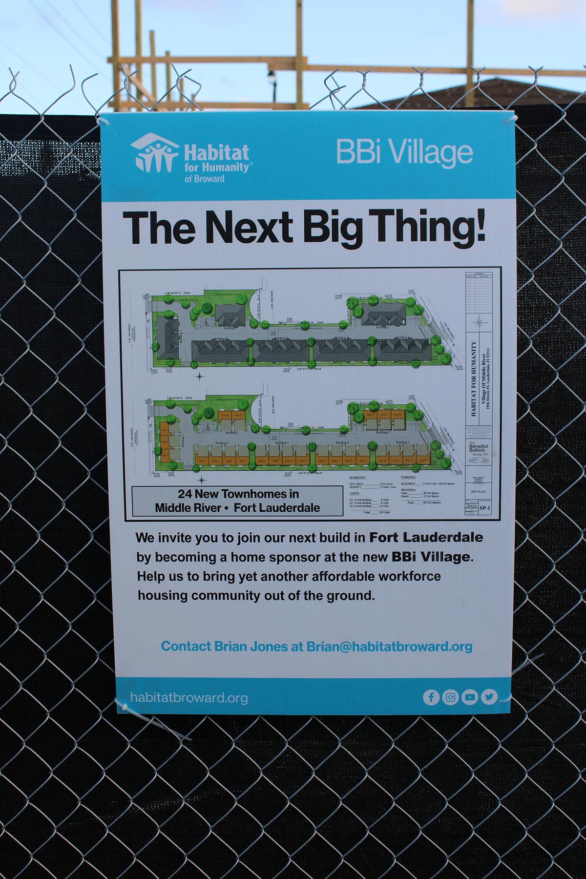 Close view of a poster on a fence reading BBi Village The Next Big Thing, with a site plan of 24 townhomes.