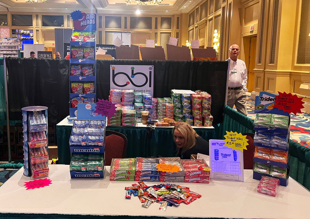 Booth table with Airheads and Mentos displays, a Trident Vibes rack and a woman bending down behind the table.