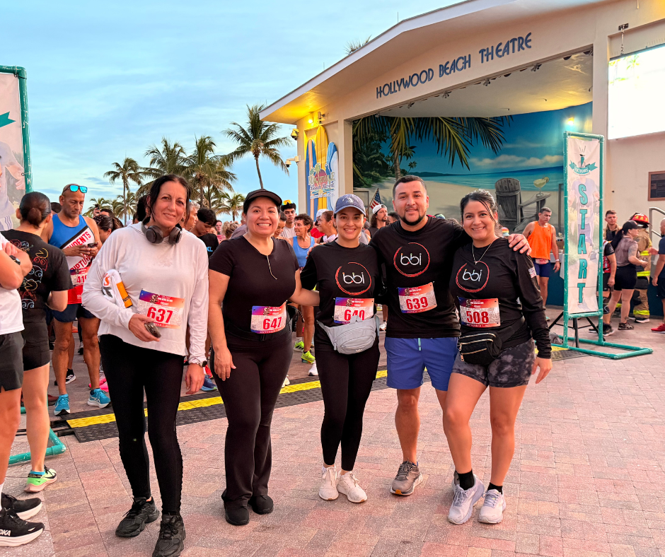 Five people in bibs, three in black bbi shirts, stand near a Start sign in front of the Hollywood Beach Theatre.