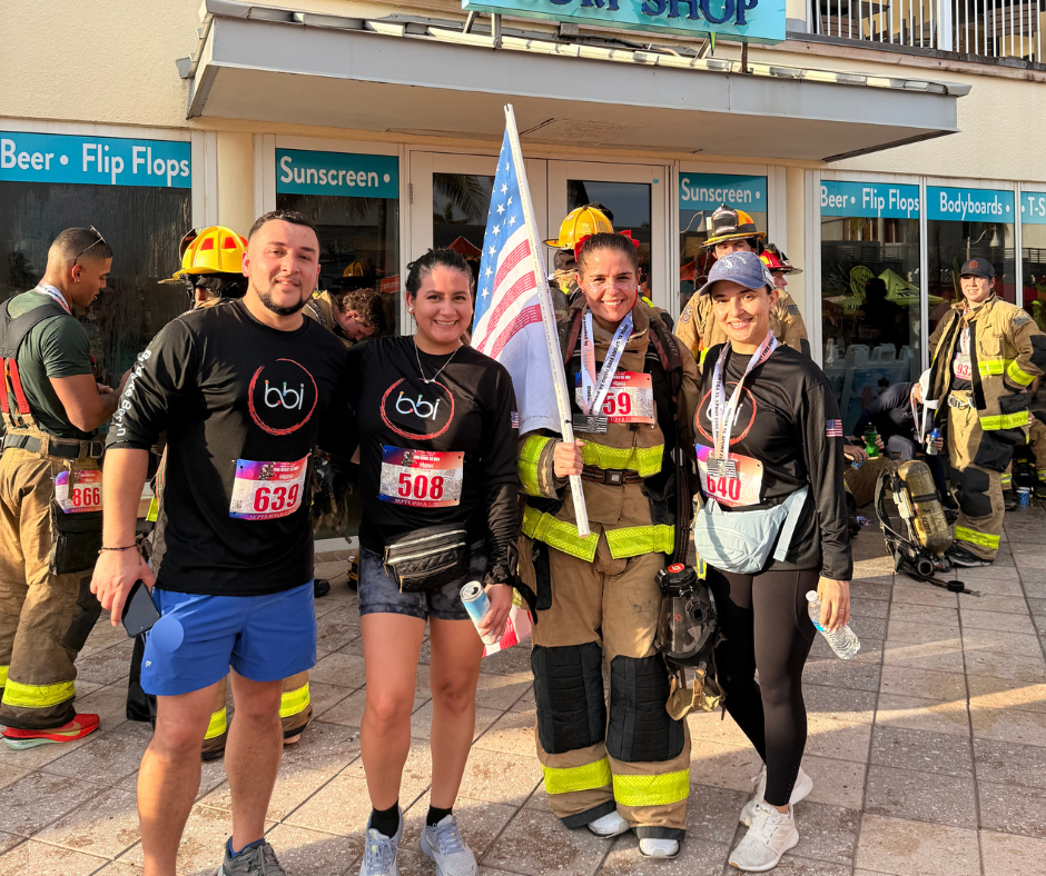 Three people in bbi shirts and bibs pose with a firefighter holding a flag in front of beachfront shops.