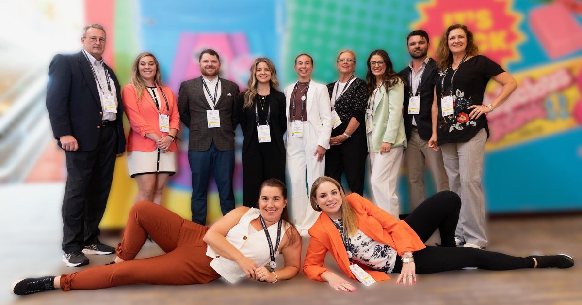 Group of adults with badges pose before a colorful mural, with two women reclining on the floor in front.