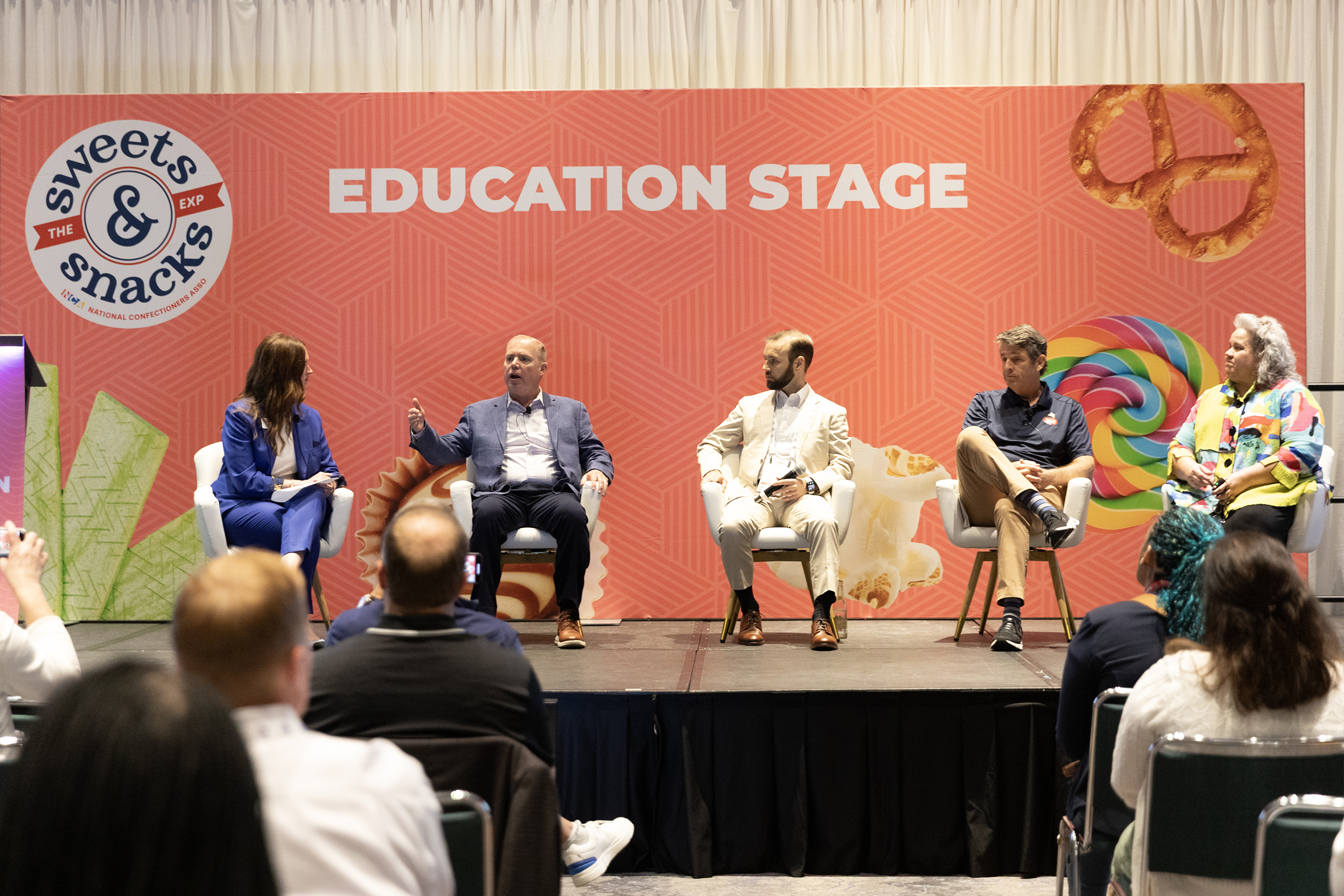 Five speakers sit in armchairs on a stage reading Education Stage, in front of a seated audience.