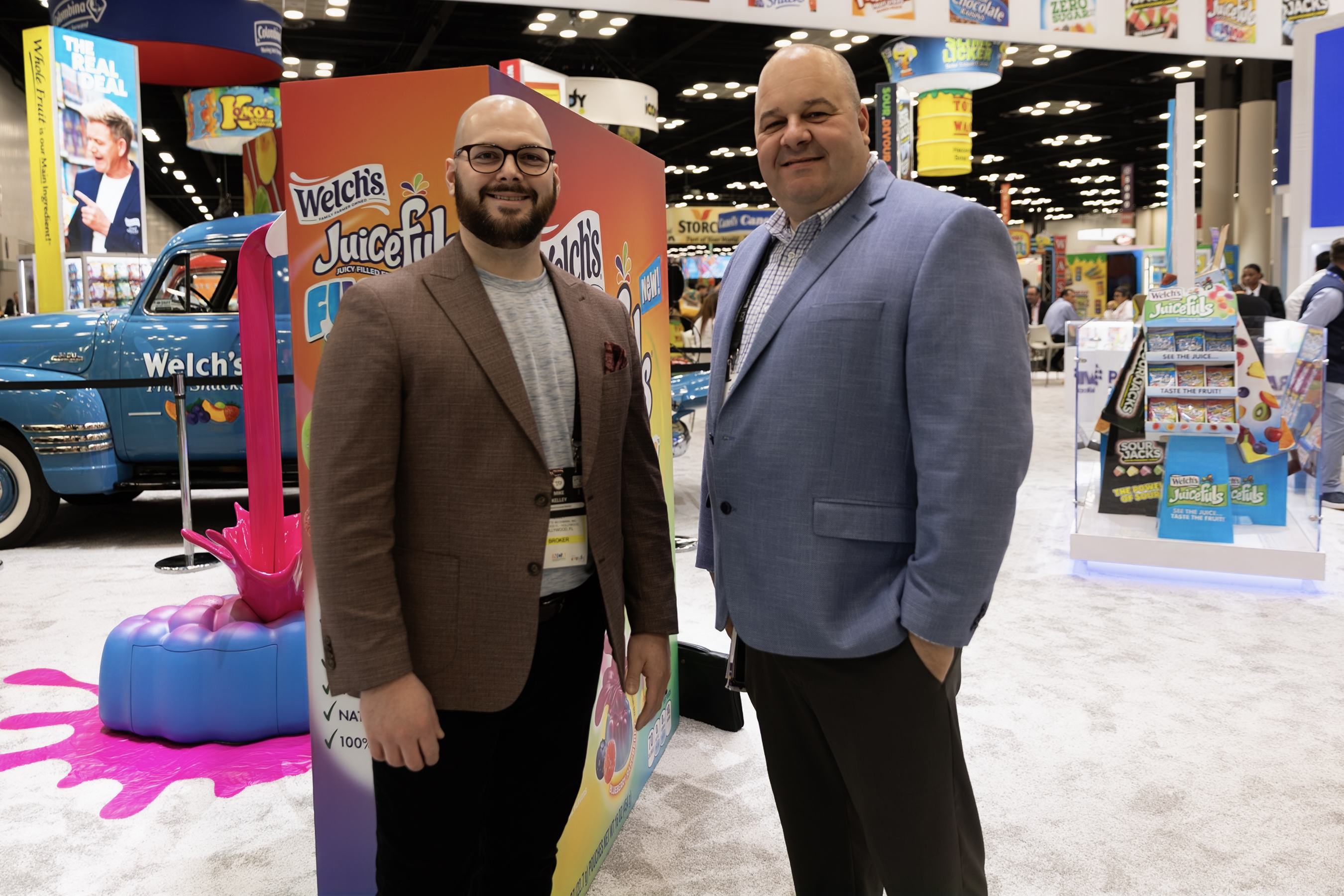 Two men pose in front of a Welch's Juicefuls display and a blue Welch's truck in an expo hall.