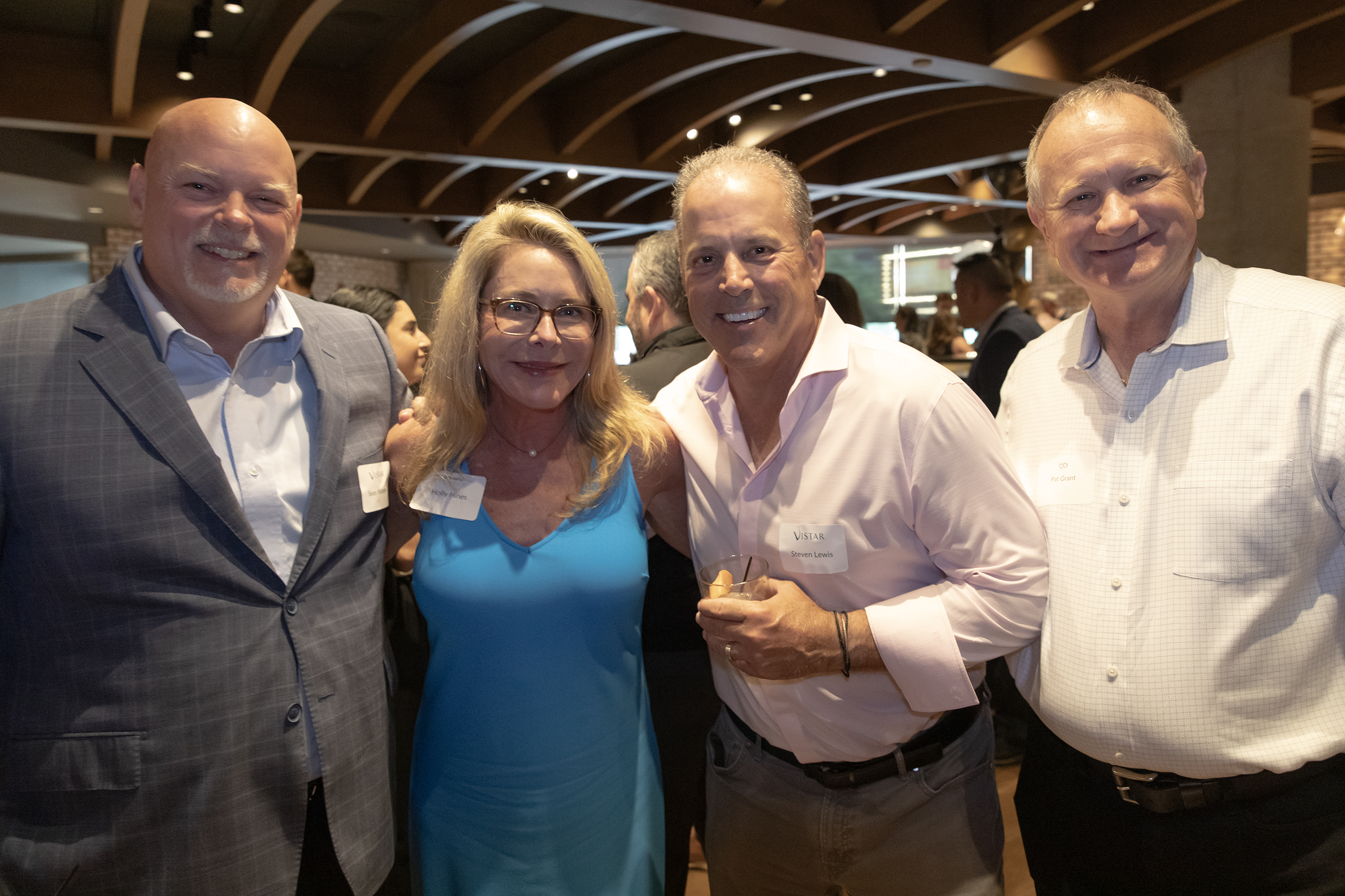 Three men and a woman with name tags pose close together at a crowded dinner reception.