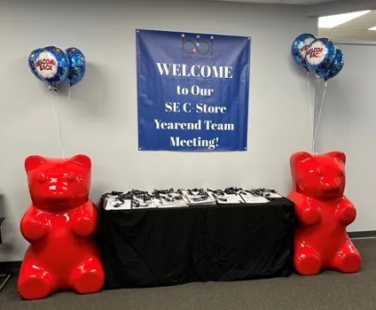 Welcome to Our SE C-Store Yearend Team Meeting banner above a black table, flanked by two giant red gummy bear statues.