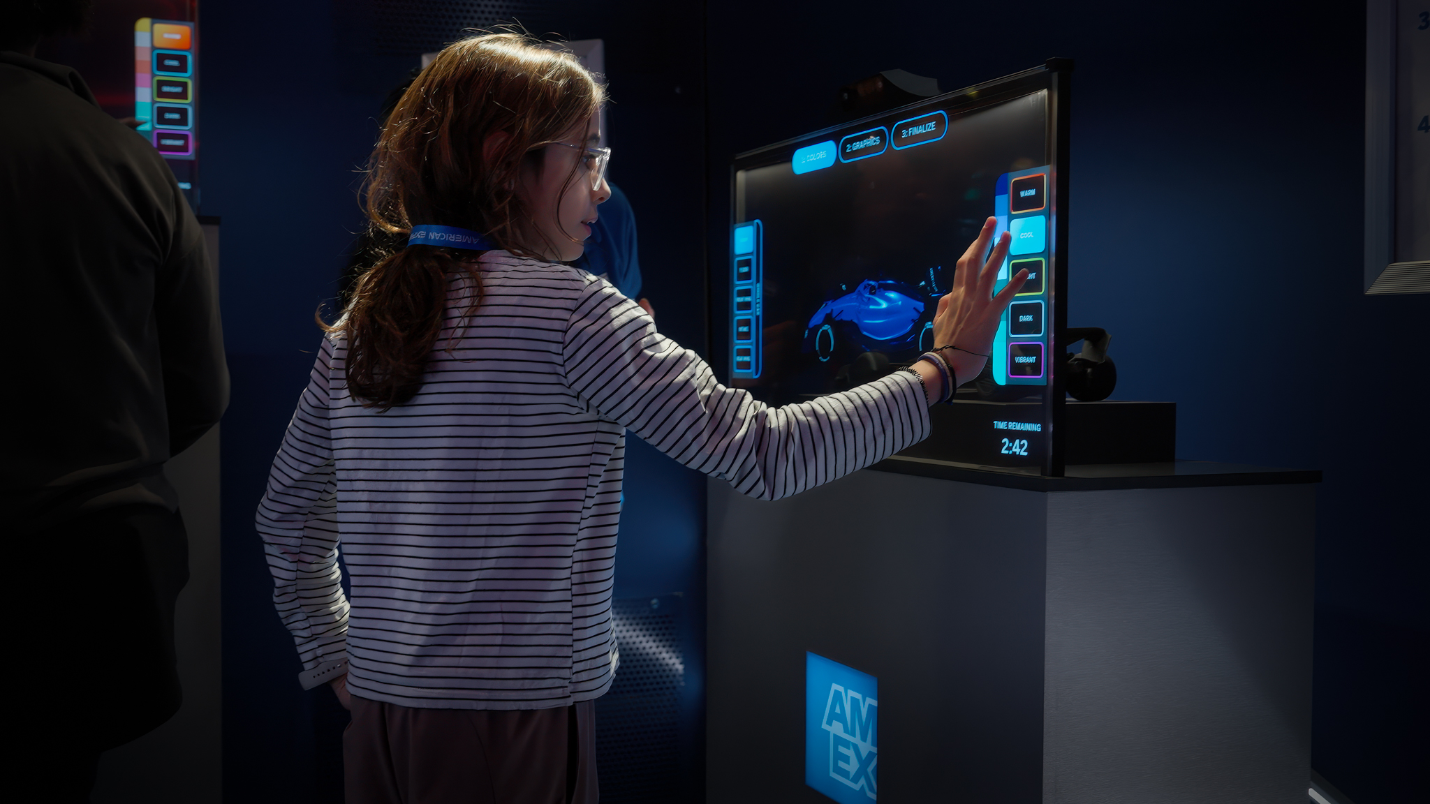 A close-up of a participant using a touchscreen to adjust a Formula 1 car livery design with illuminated background effects.