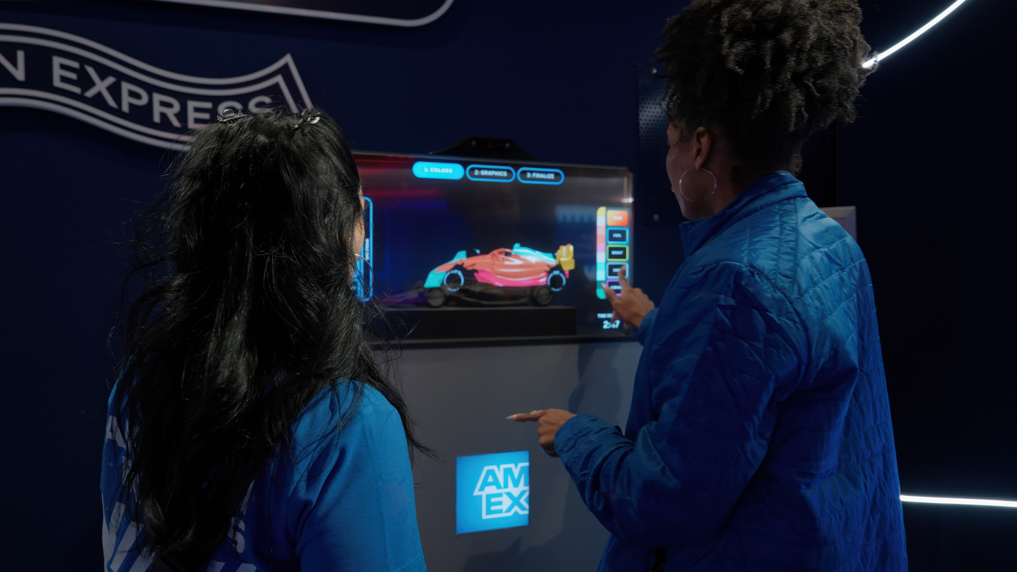 A visitor customizing a Formula 1 car livery on a touchscreen kiosk with step-by-step instructions displayed in the center.