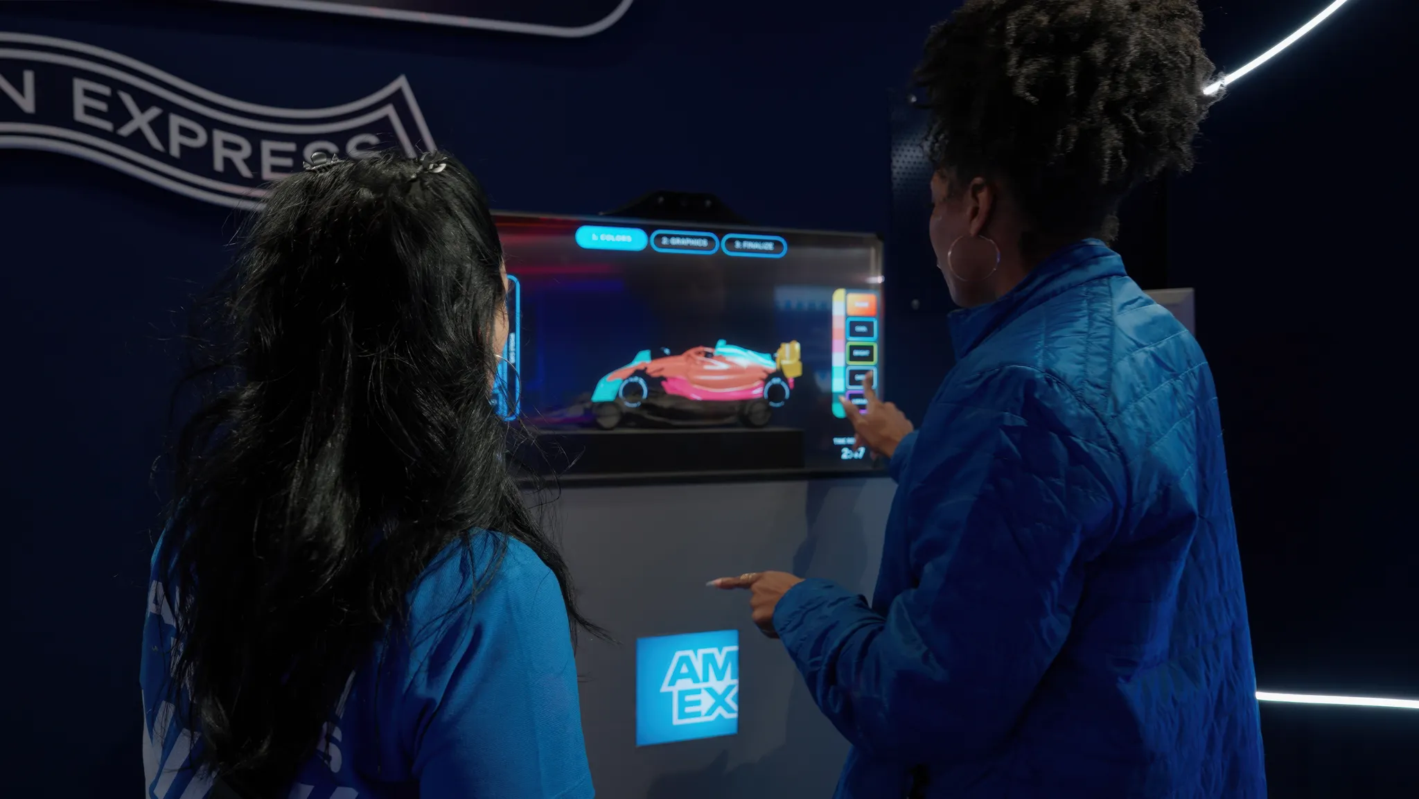 A visitor customizing a Formula 1 car livery on a touchscreen kiosk with step-by-step instructions displayed in the center.