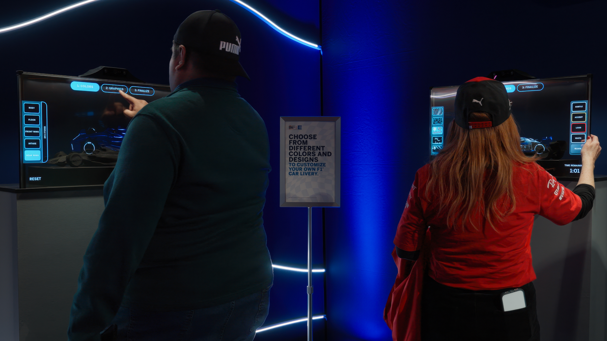 Two attendees standing at interactive kiosks, customizing their Formula 1 car liveries at an event activation.