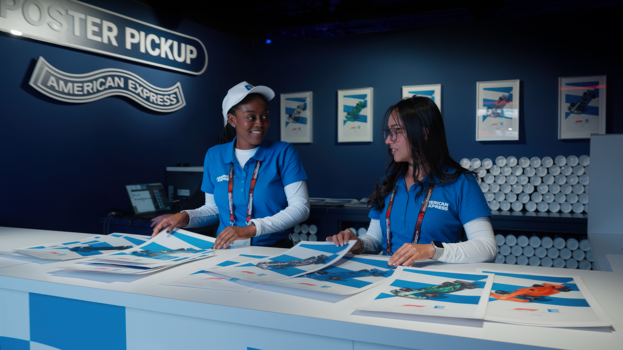 Two American Express event staff preparing custom printed posters of personalized Formula 1 car liveries for attendees.