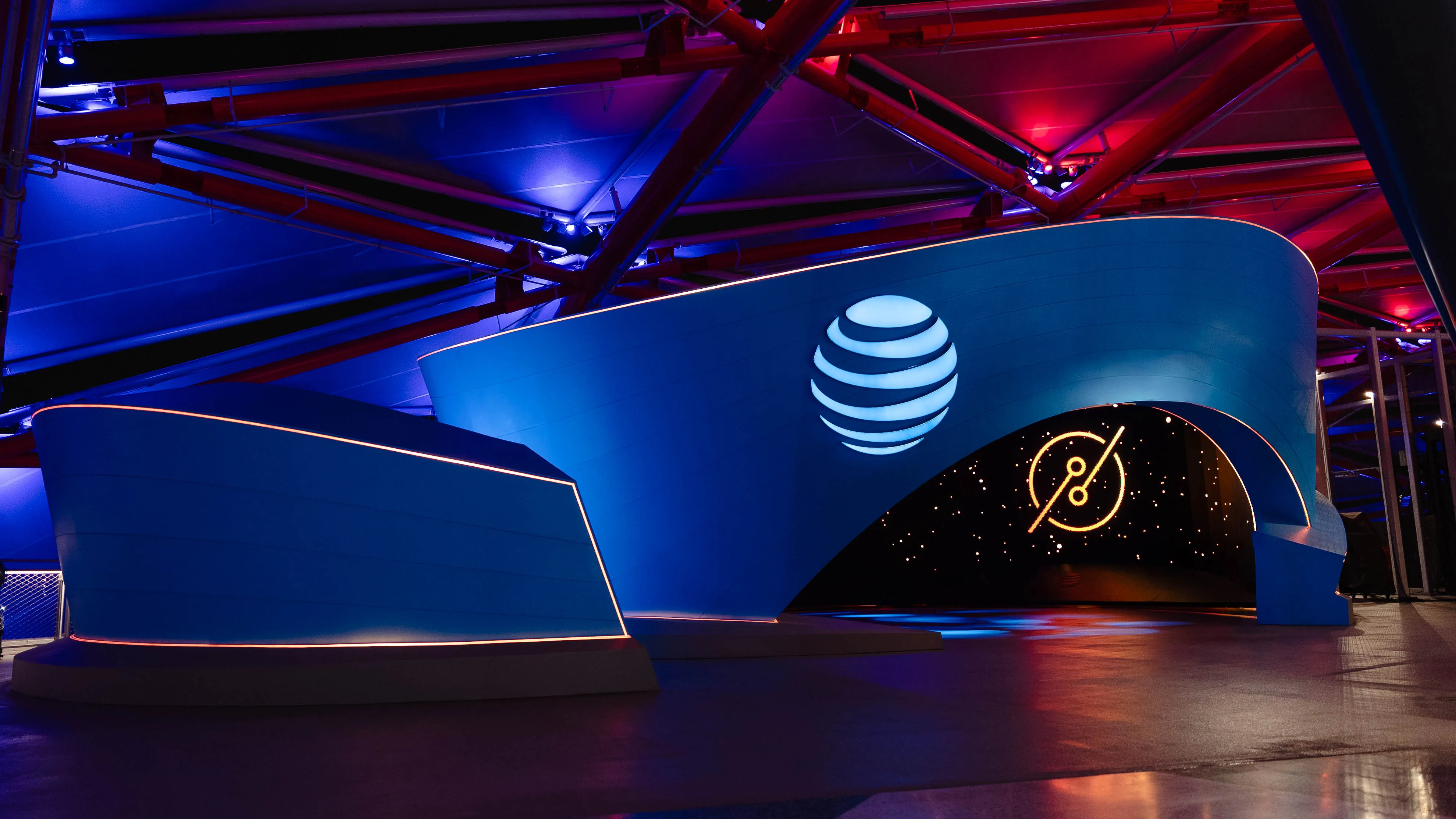 Blue AT&T-branded installation with curved architectural forms, illuminated signage, and colorful lighting reflecting across the floor. Luminary logo is displayed on a big screen.