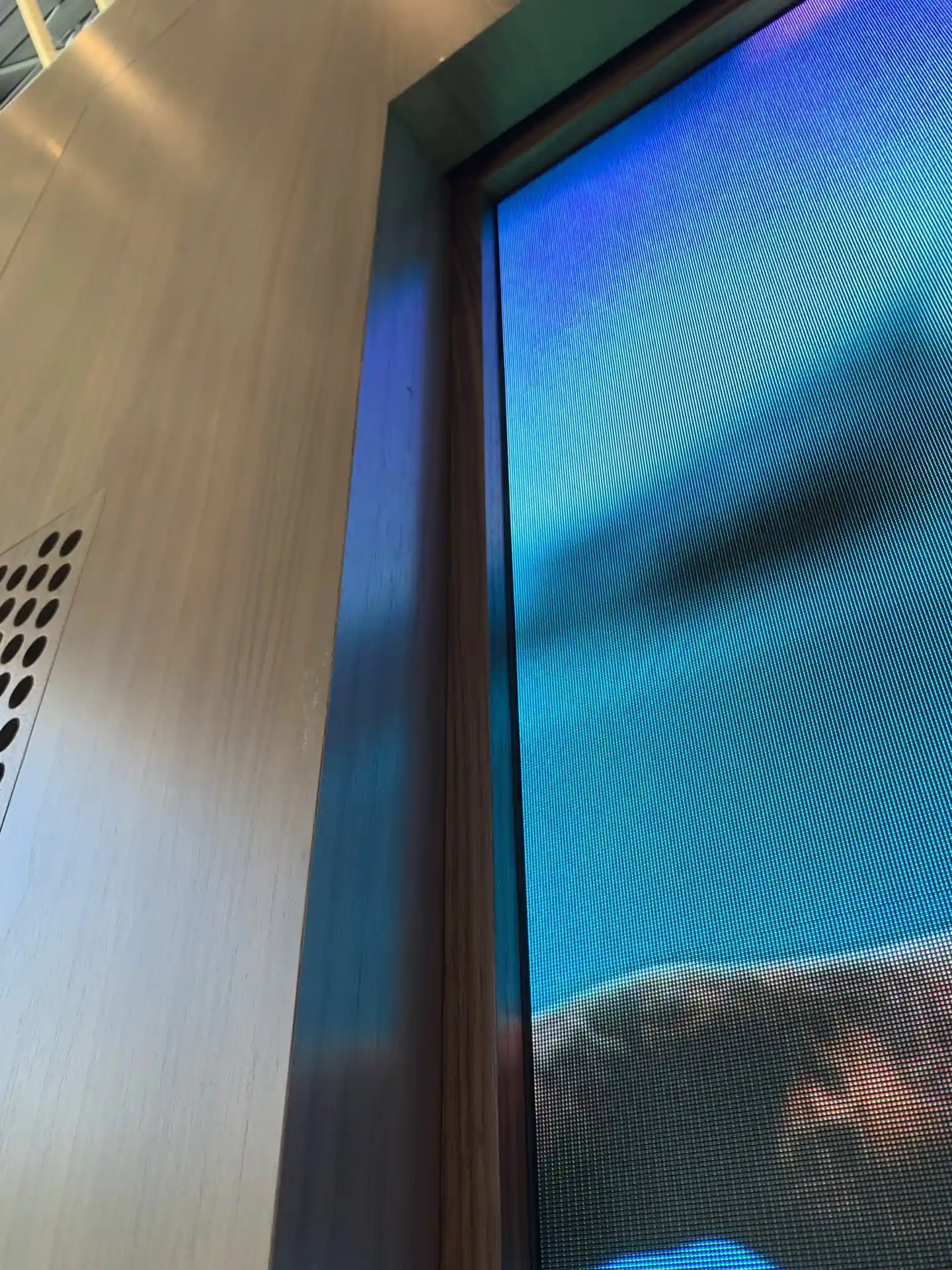 Close-up of a digital screen with vibrant blue and green hues, set against a wooden wall with perforated patterns.