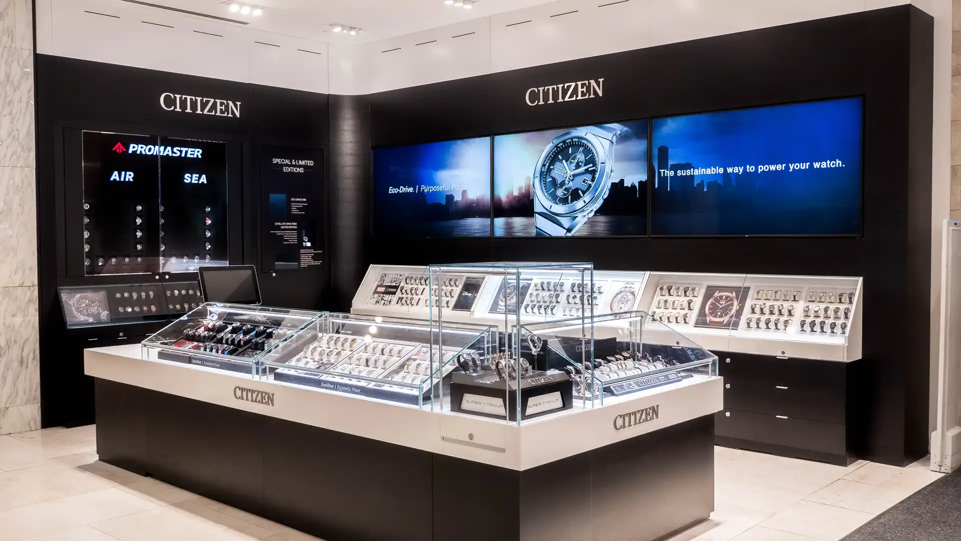Citizen Watch retail display cases beneath digital screens at Macy’s Herald Square.
