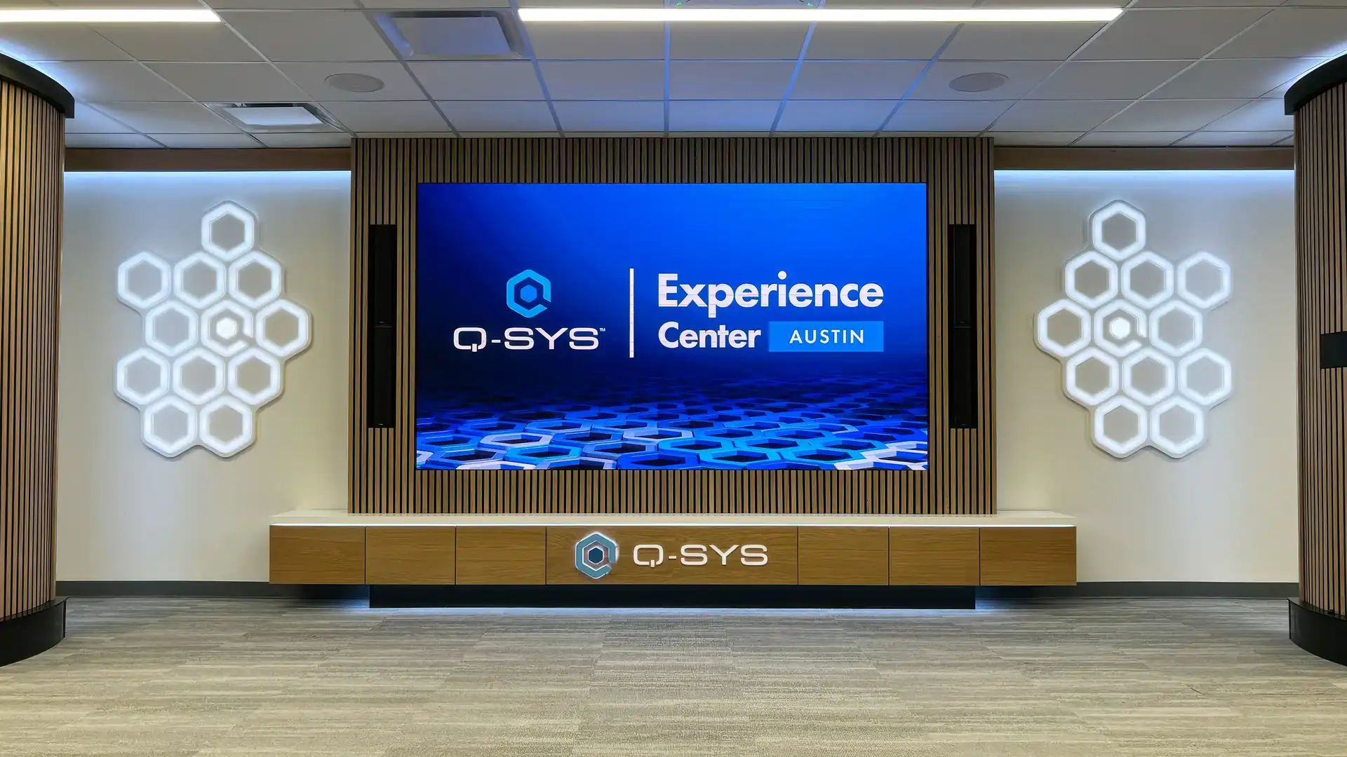 Q-SYS Austin Experience Center with a central LED display, custom woodwork, and illuminated wall graphics.