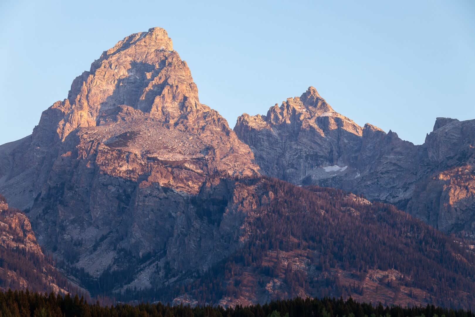 The mountain peak of Grand Teton lit up at sunrise with colorful pink and purple hues