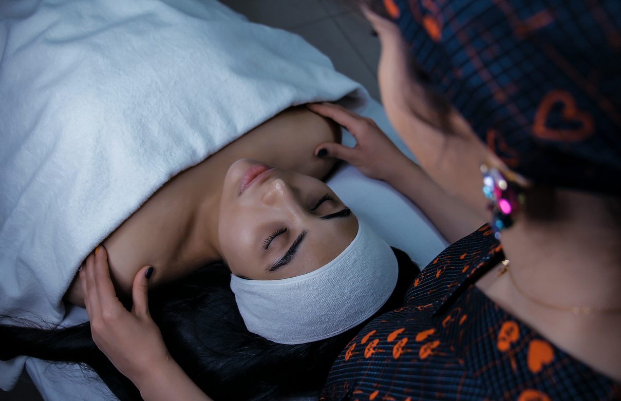 Esthetician performing a facial massage on a client wearing a spa headband