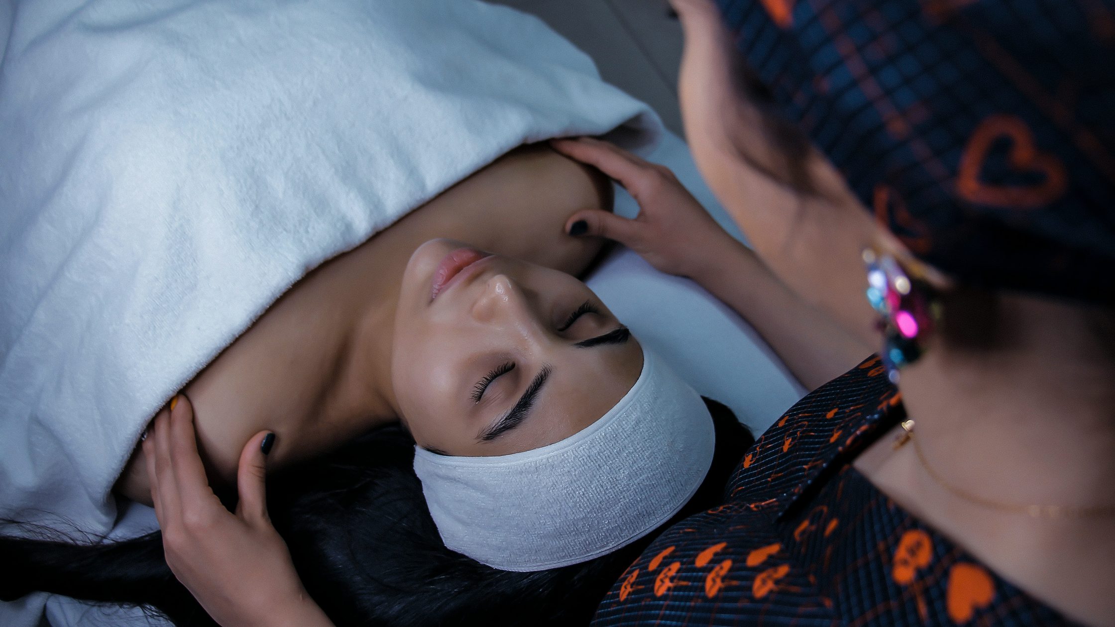 Esthetician performing a facial massage on a client wearing a spa headband