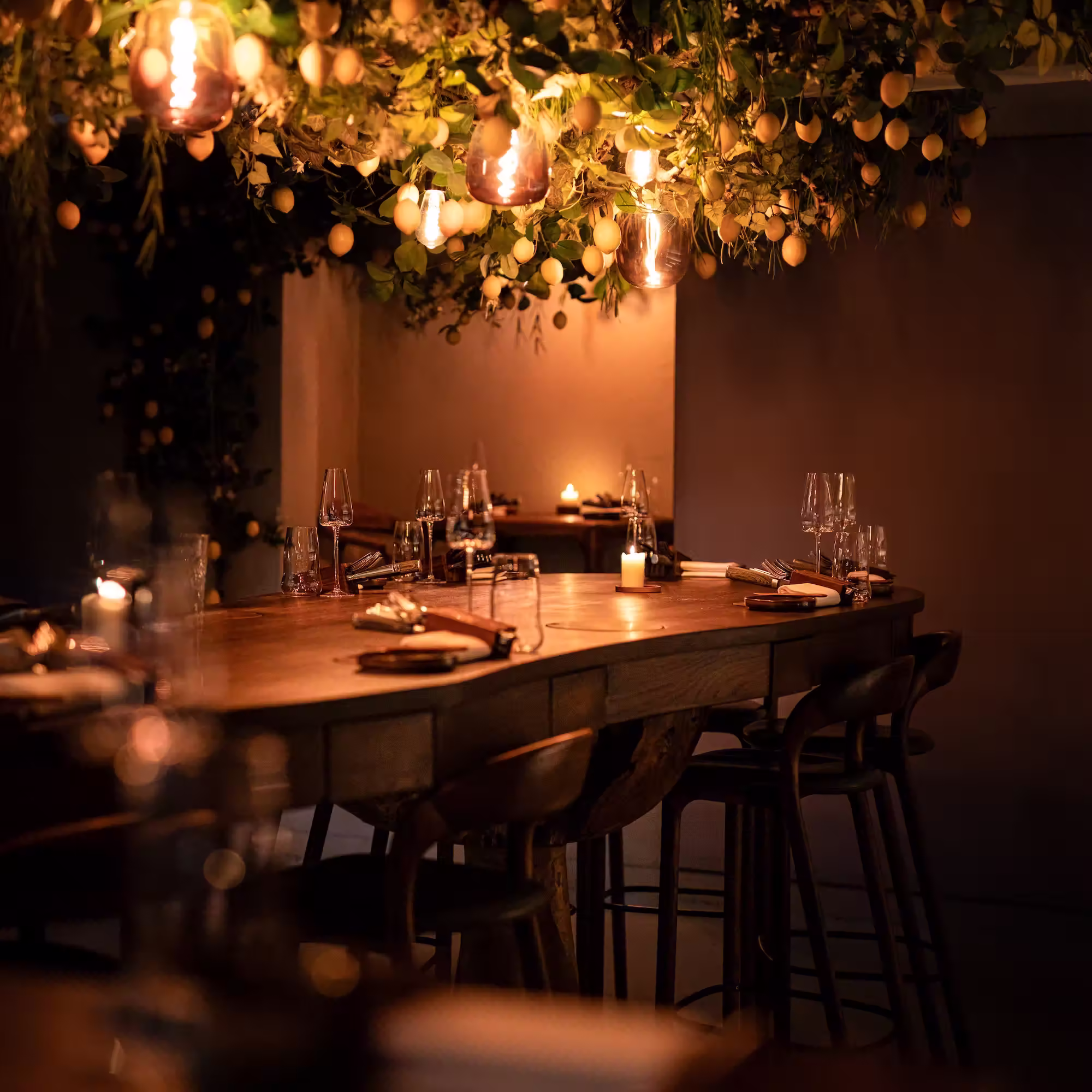 Gezellig restaurantinterieur met houten tafel, kaarsen, glazen en hanging limoen- en plantendecoratie.