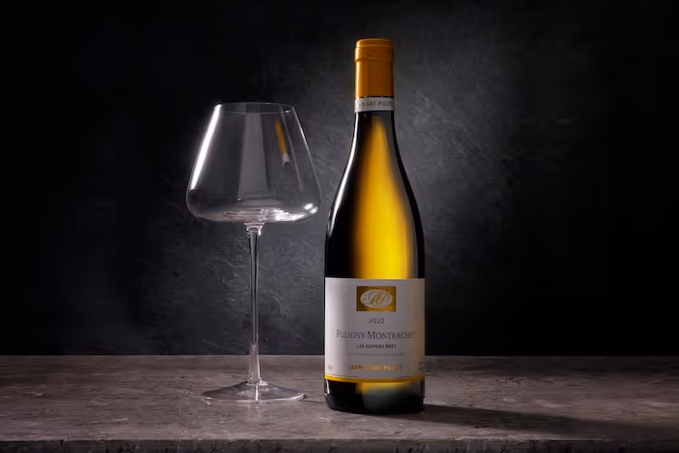 Fles witte wijn naast een leeg wijnglas op een donkere achtergrond.