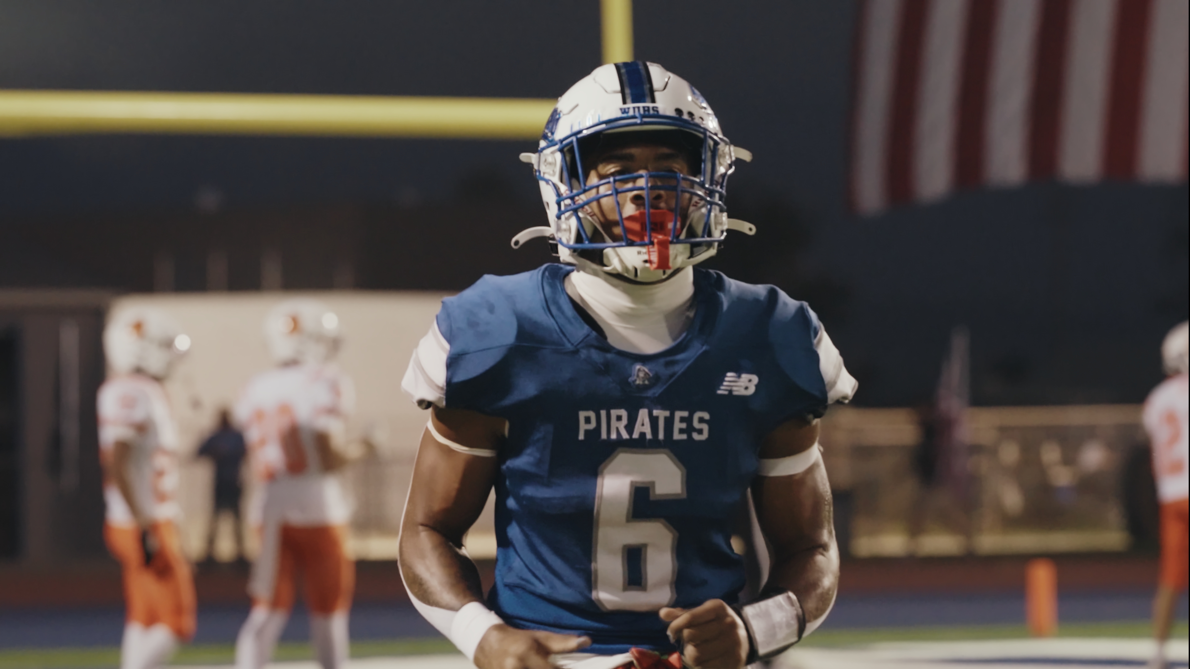 Football player wearing a blue Pirates jersey number 6 and white helmet on the field at night.