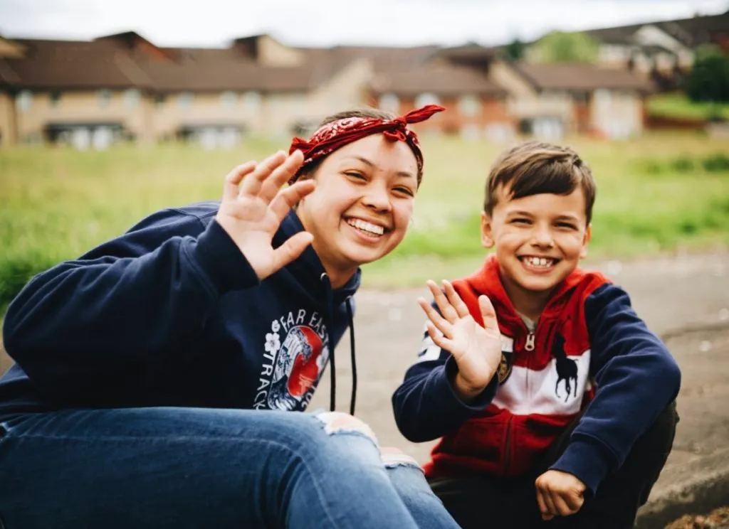 A Royal Servants participant and a local smiling and waving to a camera.