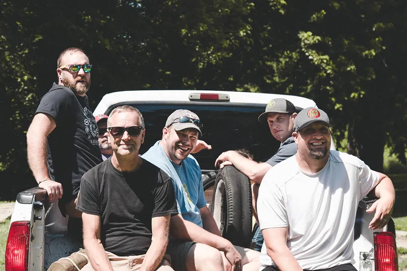 A group of men sitting on the back of a work truck.