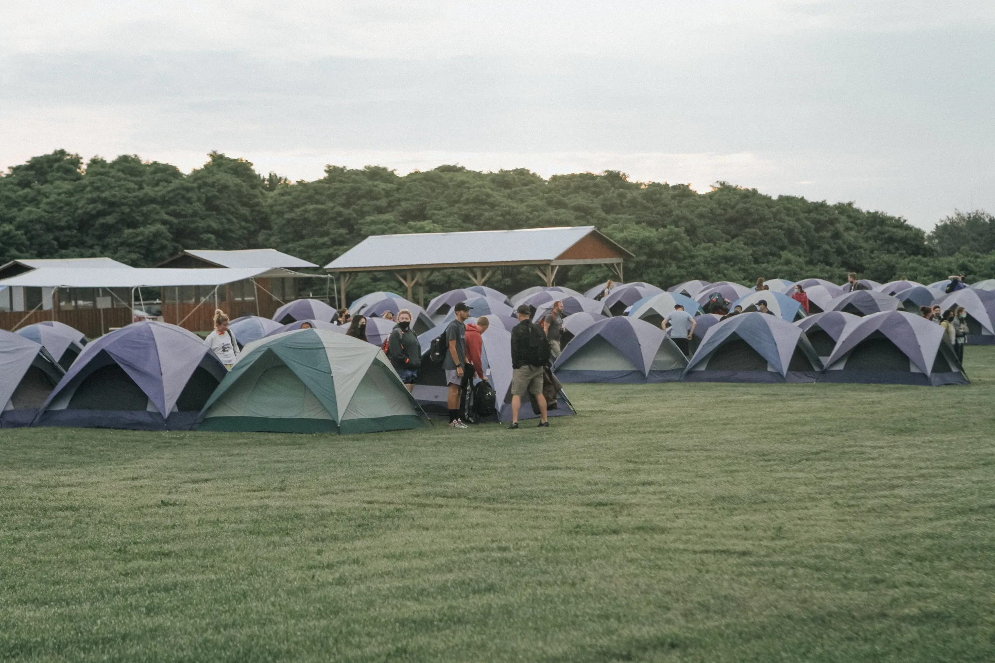 A field with rows of blue tents with people slowly lining up at the end of them.