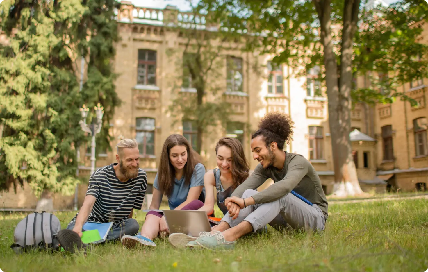 Group of college students sitting on campus lawn with a laptop, representing different ways students use HiHello digital business cards for networking, dorm life, clubs, side hustles, and career fairs.