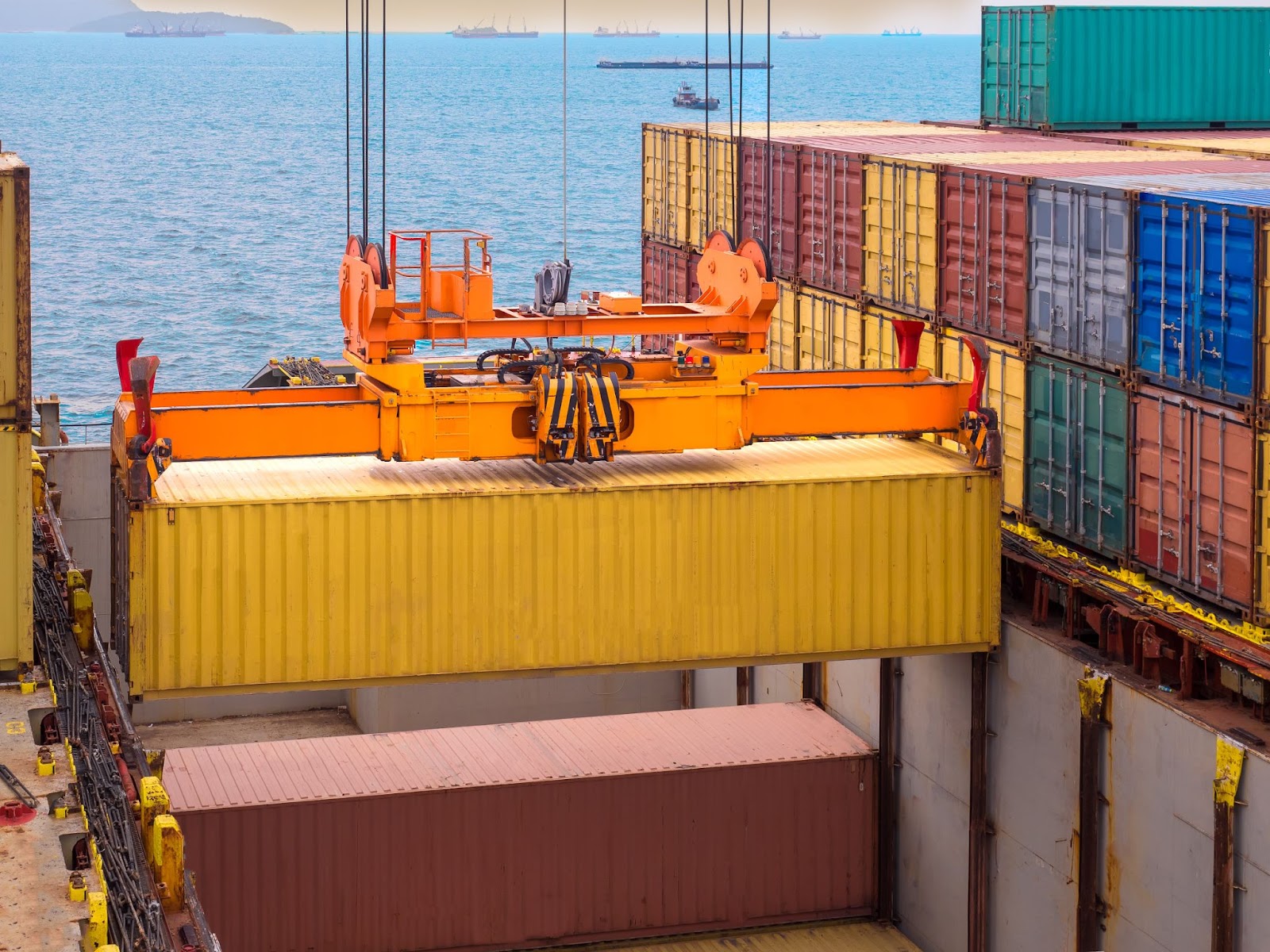 Alt text: A yellow container is being lifted from the vessel by a port crane.