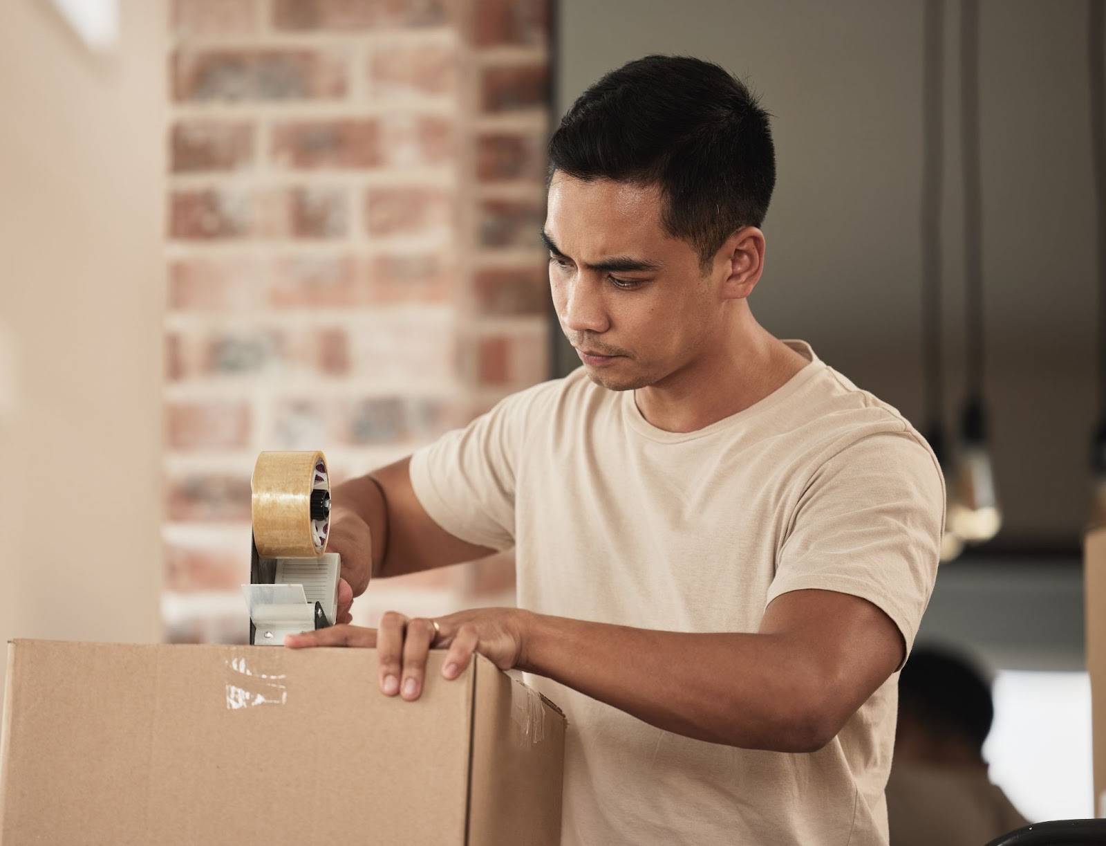 Alt text: A man is sealing the flaps of a box with packaging tape. 