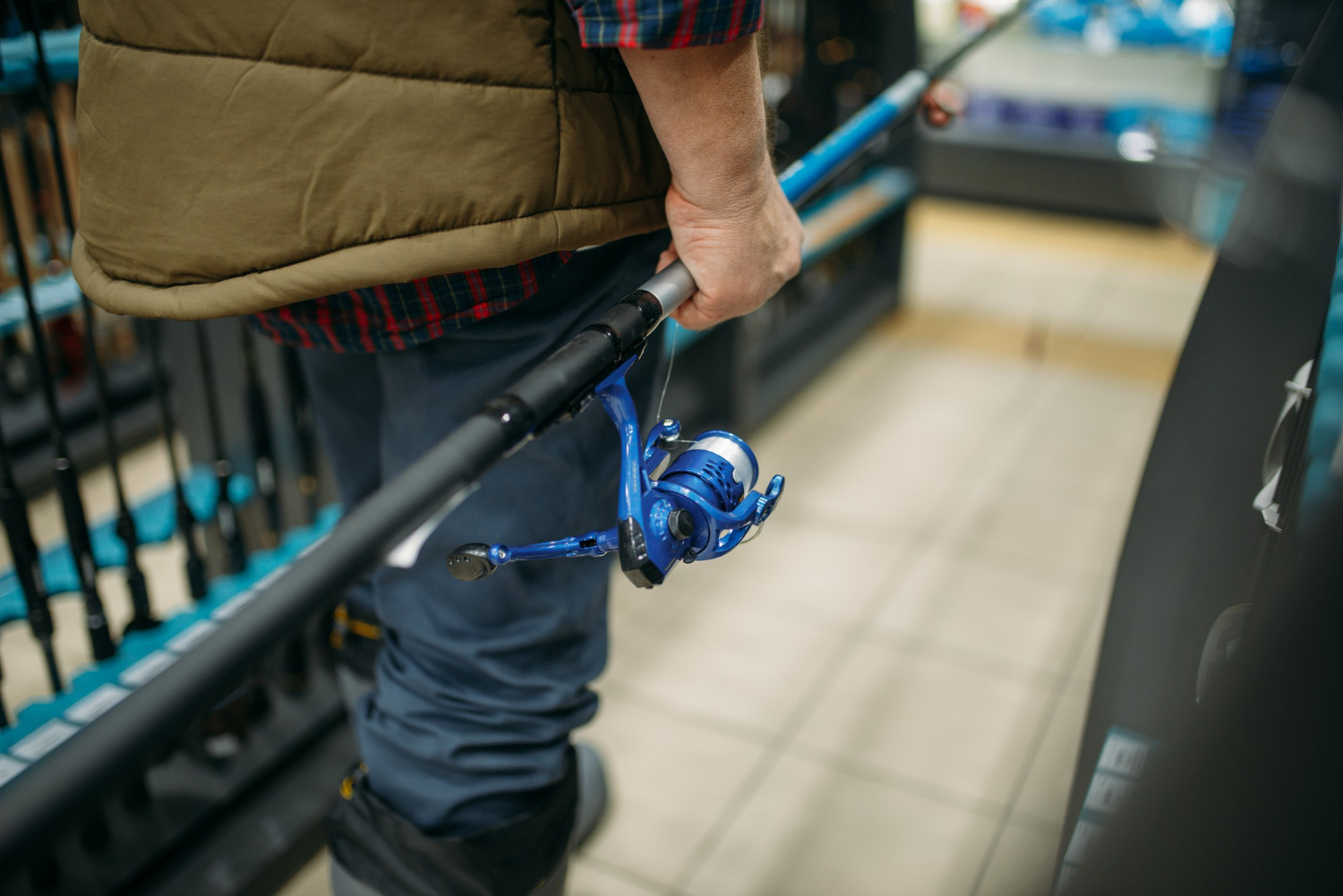 Alt text: A fisherman is holding a fishing rod while walking down an aisle of a shop.